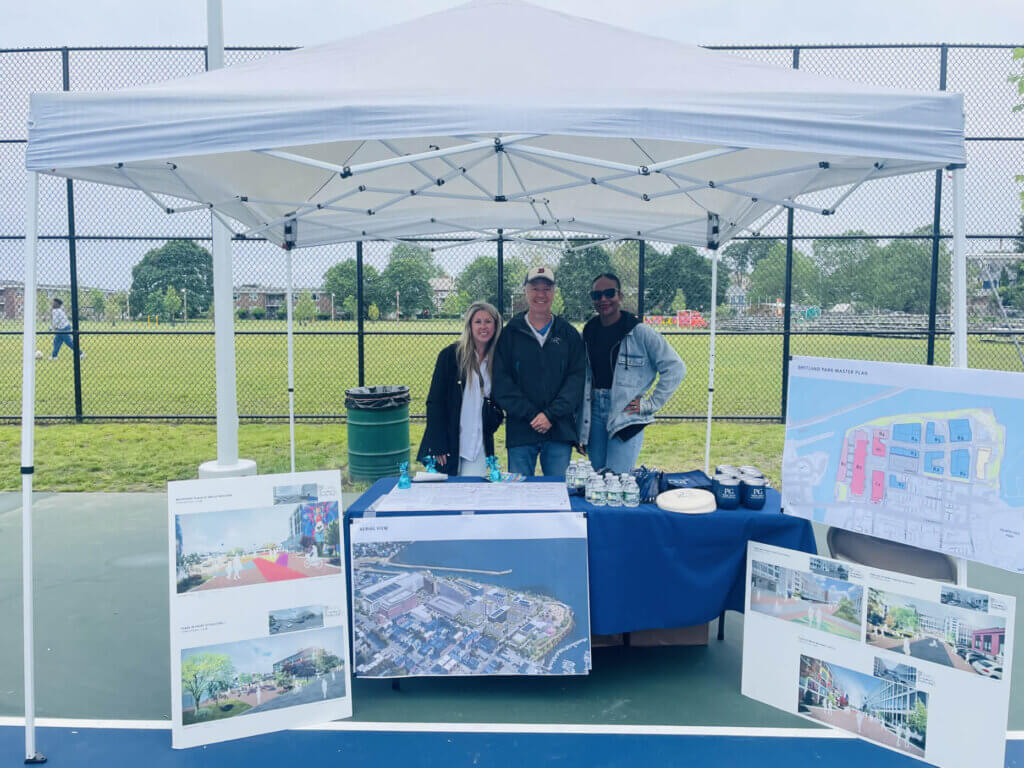 Three people posing behind a table that showcases photos of a proposed reconstruction project.